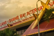 Chiang Rai Airport building with palm trees and cloudy sky in the background.