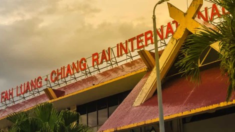 Chiang Rai Airport building with palm trees and cloudy sky in the background.