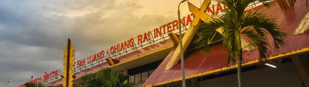 Chiang Rai Airport building with palm trees and cloudy sky in the background.
