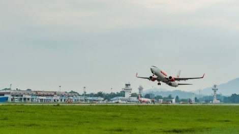 Airplane taking off from Chiang Rai Airport with control tower and terminal in background.
