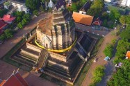 Aerial view of a historic temple with a central chedi in Chiang Mai, Thailand, surrounded by trees.