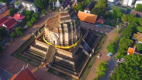 Aerial view of a historic temple with a central chedi in Chiang Mai, Thailand, surrounded by trees.