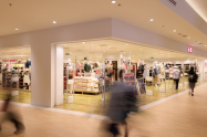 Inside a shopping mall with stores and shoppers walking around.